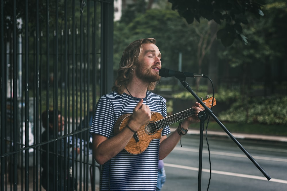 man holding ukulele standing near grills