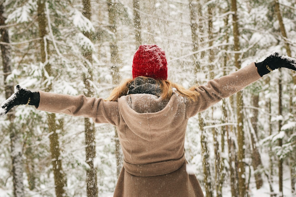 パーカーを着た女性が雪の降る木々の近くで腕を広げる