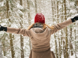 woman wearing hoodie spreading her arm near trees with snows
