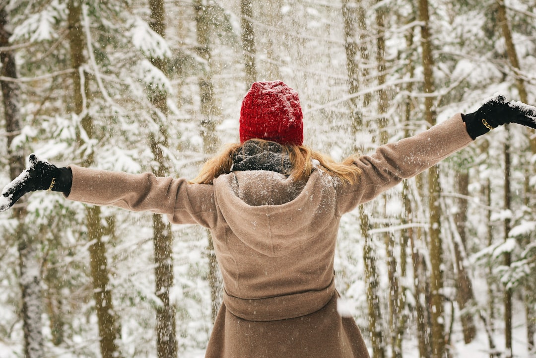woman wearing hoodie spreading her arm near trees with snows,