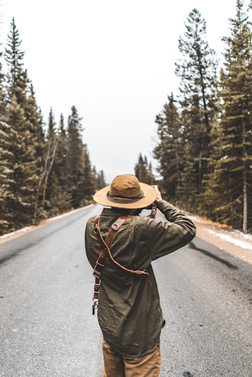 person taking photograph of road between trees