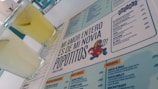 A menu with a distinctive quote and colorful cartoon graphic is prominently featured. Two glasses filled with a light yellow beverage are placed next to the menu. The layout includes sections with lists of food and drinks, indicating a restaurant or cafe setting.