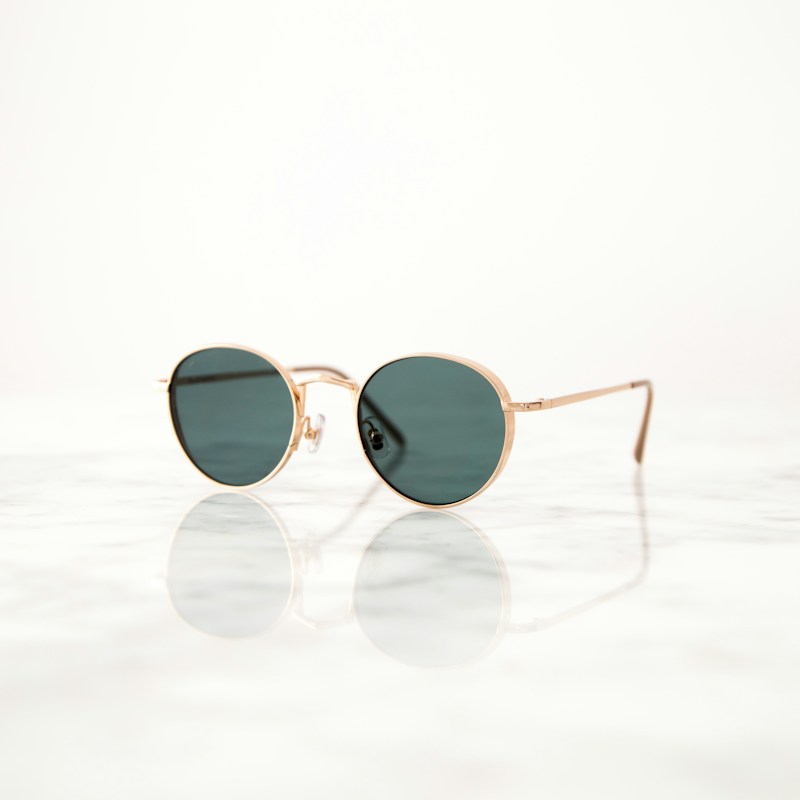 Gold round sunglasses with green lenses on a white surface