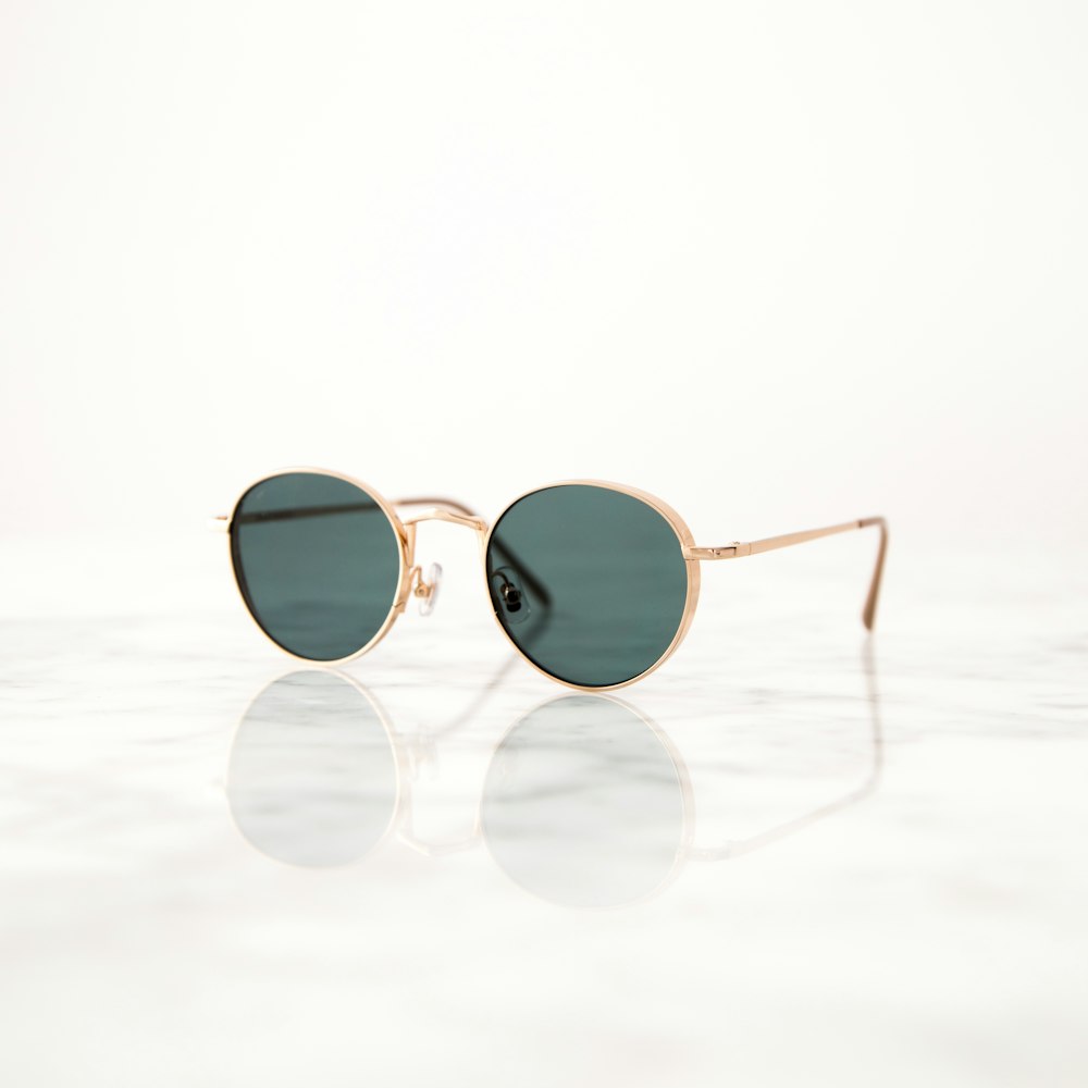 óculos de sol hippie emoldurados dourados na superfície branca
