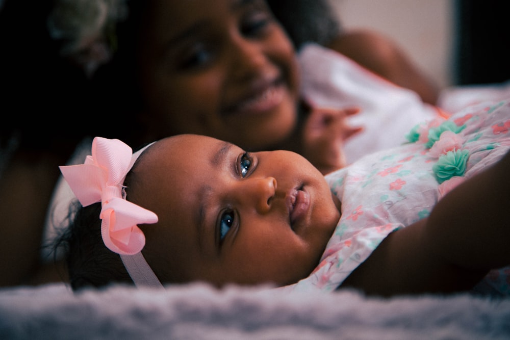 toddler wearing white and pink headdress lying near girl