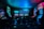 Dimly lit gaming arcade featuring a variety of brightly illuminated slot machines and video gaming screens. Neon signs and colorful displays create a vibrant atmosphere. The arrangement of gaming machines suggests an inviting space for entertainment, with chairs positioned for players.