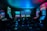Dimly lit gaming arcade featuring a variety of brightly illuminated slot machines and video gaming screens. Neon signs and colorful displays create a vibrant atmosphere. The arrangement of gaming machines suggests an inviting space for entertainment, with chairs positioned for players.