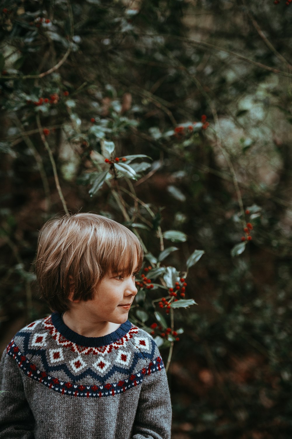 boy standing in front of plants with red berries during daytime