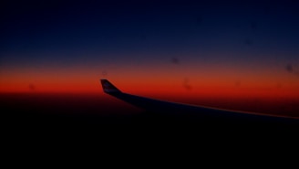 A dark blue sky transitions into a vibrant orange and red horizon, with the silhouette of an airplane wing visible in the foreground.