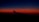 A dark blue sky transitions into a vibrant orange and red horizon, with the silhouette of an airplane wing visible in the foreground.
