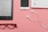 A pair of red reading glasses, an e-reader displaying a page in Spanish, white earphones, a smartphone, and a planner open to the page showing '24th' are neatly arranged on a pink surface.