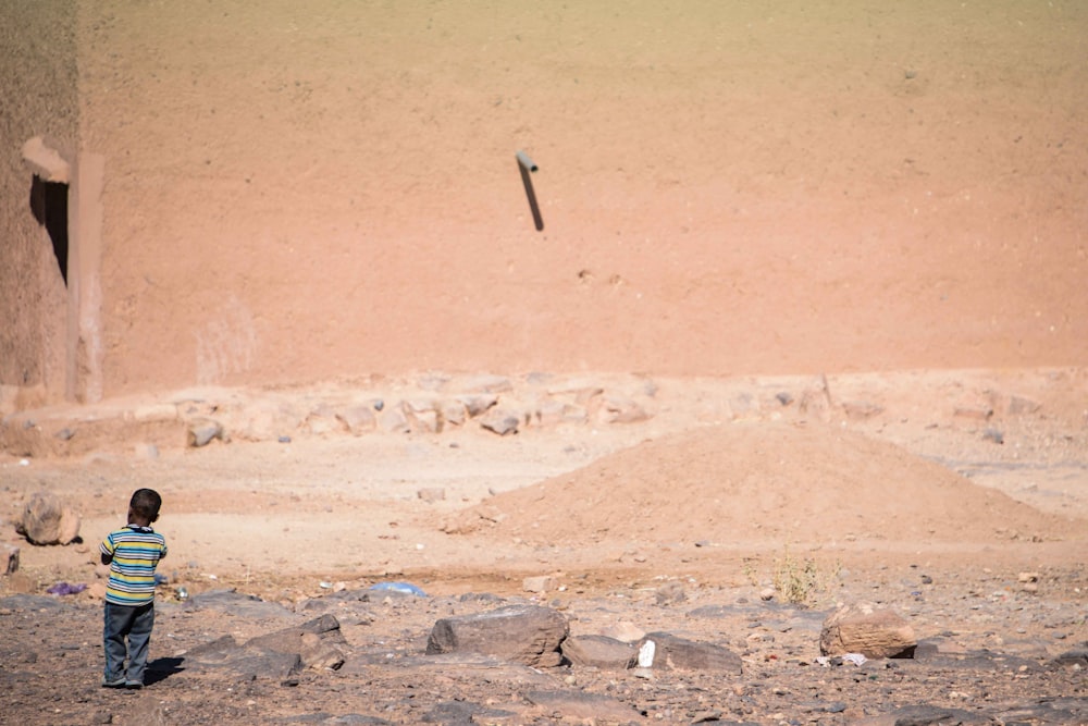 toddler standing near pile of sand at daytime