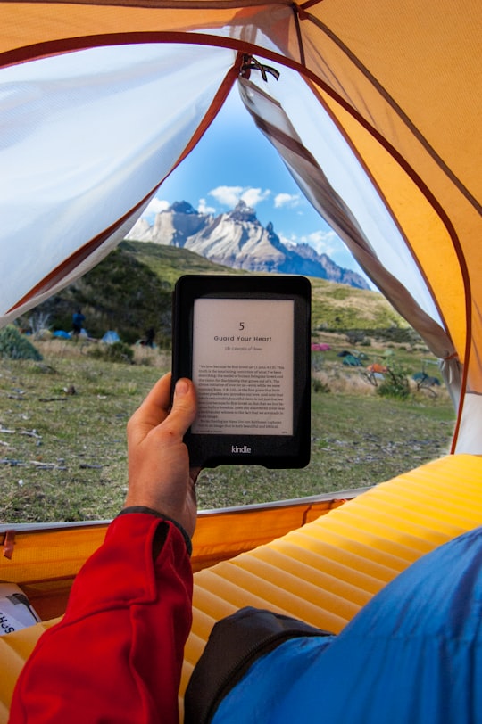 person holding black Amazon Kindle E-Book reader inside tent at daytime in Torres del Paine National Park Chile