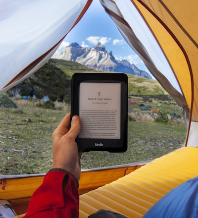 person holding black Amazon Kindle E-Book reader inside tent at daytime