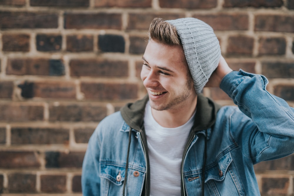 man holding the back of his head while smiling near brick wall