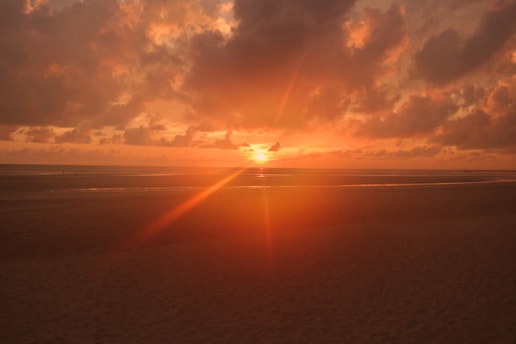 A vibrant sunset over a serene beach with a lone traveler gazing at the horizon.