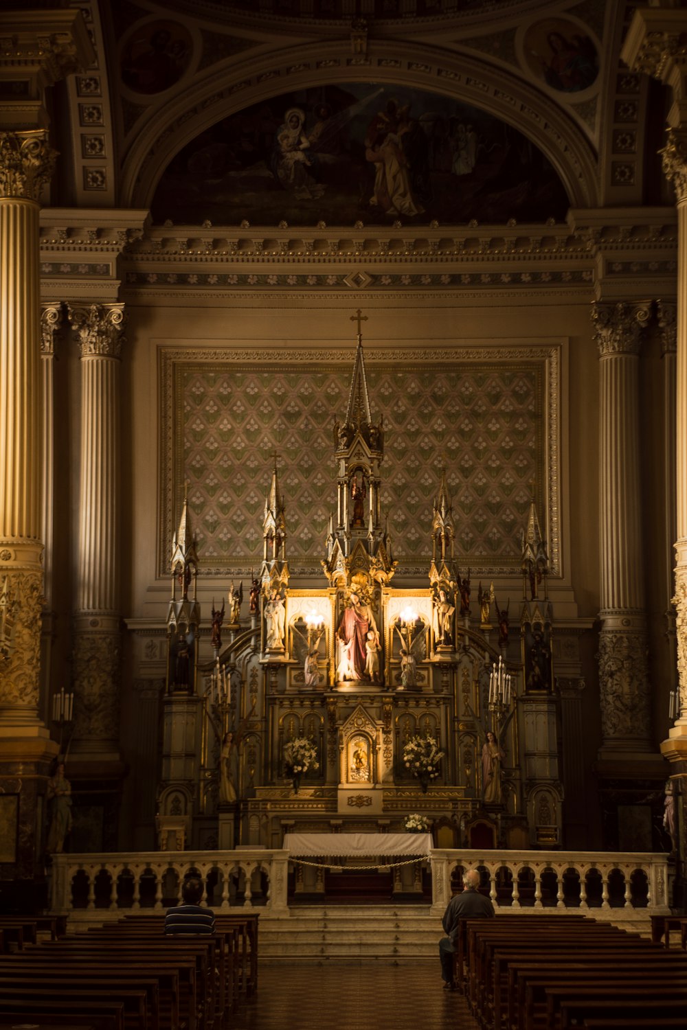 duas pessoas sentadas no banco rezando em frente ao altar