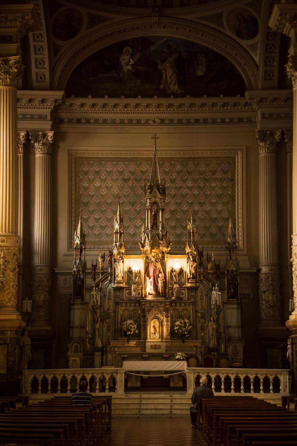 Zwei Personen sitzen auf einer Kirchenbank und beten vor dem Altar