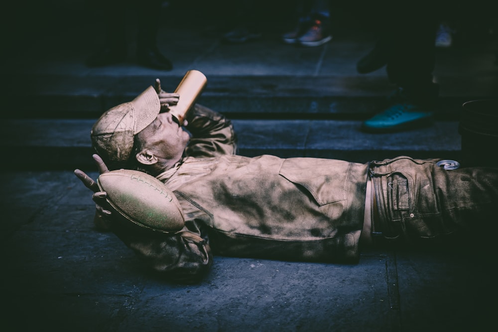 man lying down on concrete pavement holding football