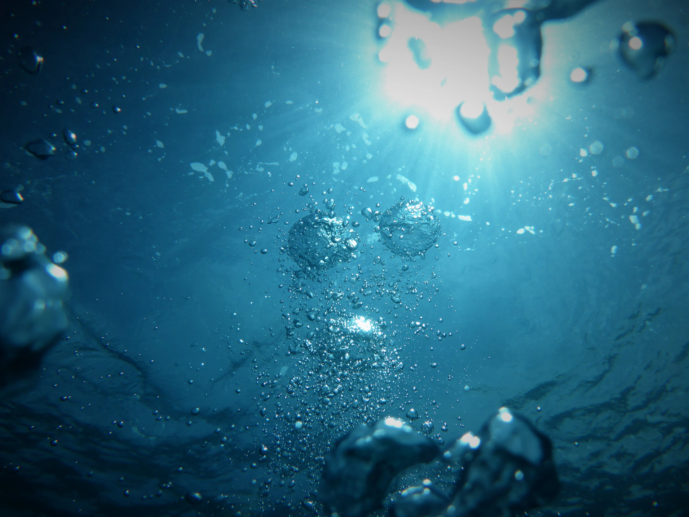Underwater view looking up at the sun with air bubbles rising through deep blue water