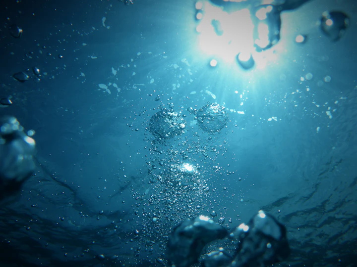 Underwater view looking up at the sun with air bubbles rising through deep blue water