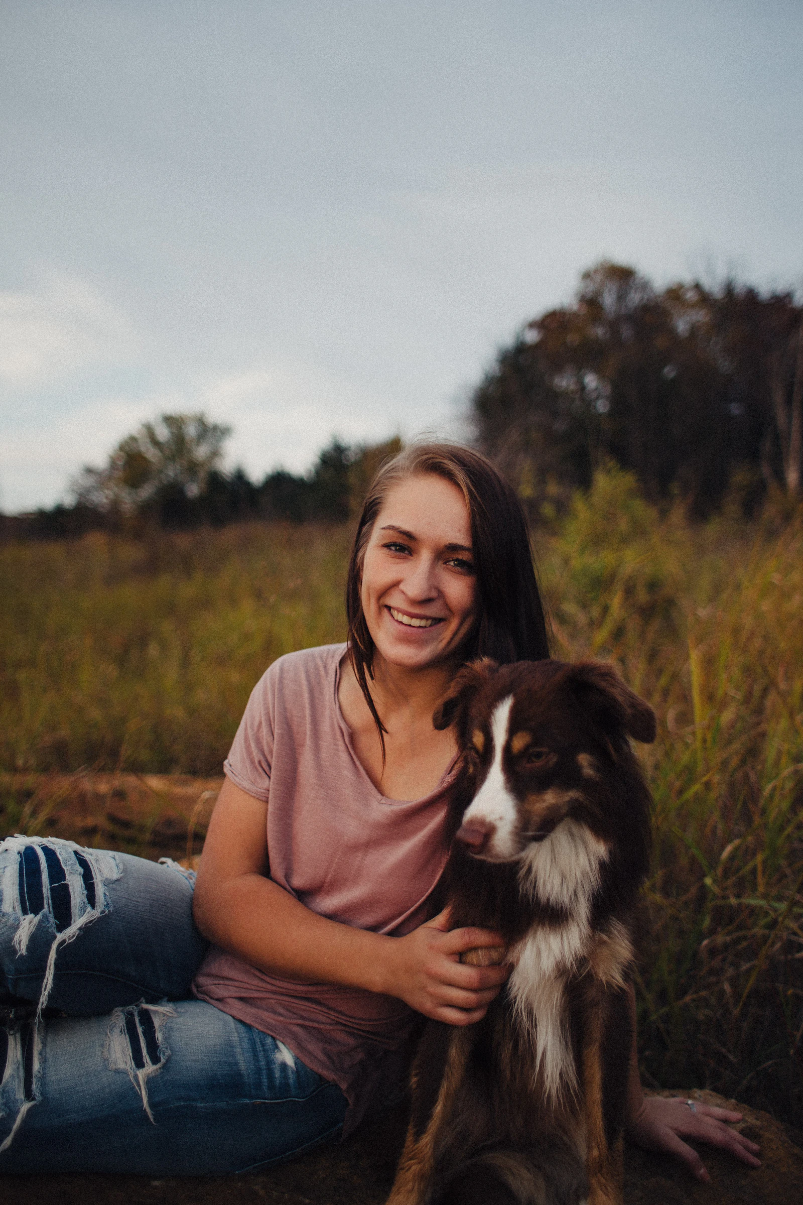 A young woman sitting outdoors beside a calm black and white dog