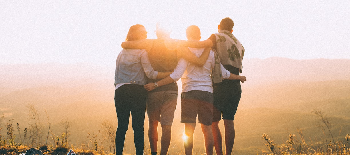 four person hands wrap around shoulders while looking at sunset