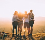 four person hands wrap around shoulders while looking at sunset