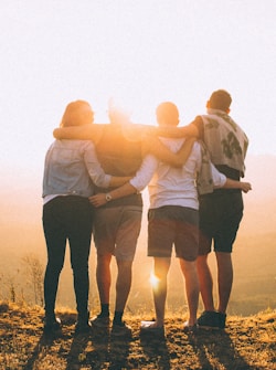 four person hands wrap around shoulders while looking at sunset