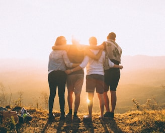 four person hands wrap around shoulders while looking at sunset