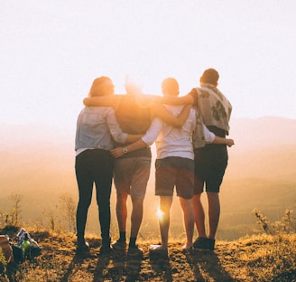 four person hands wrap around shoulders while looking at sunset