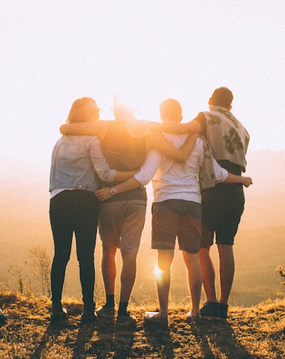 four person hands wrap around shoulders while looking at sunset