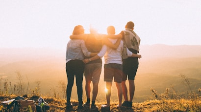 four person hands wrap around shoulders while looking at sunset