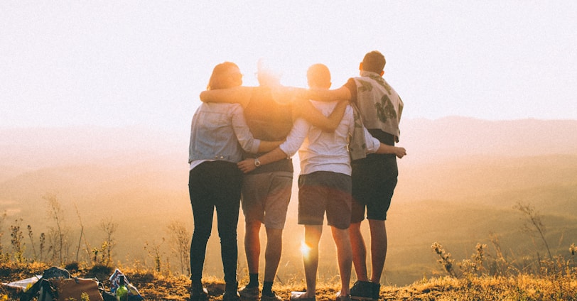 four person hands wrap around shoulders while looking at sunset