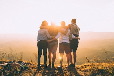 four person hands wrap around shoulders while looking at sunset hug google meet background