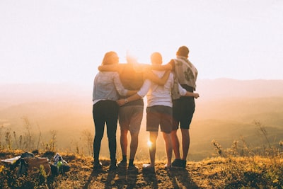 four person hands wrap around shoulders while looking at sunset friendly teams background