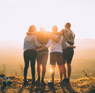 four person hands wrap around shoulders while looking at sunset