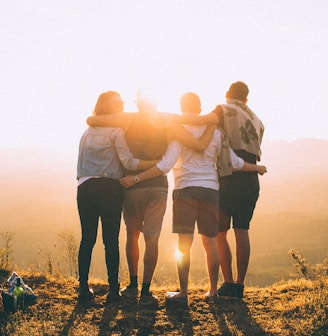 four person hands wrap around shoulders while looking at sunset