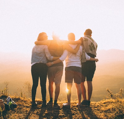 four person hands wrap around shoulders while looking at sunset