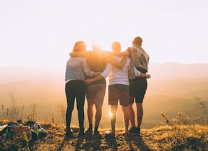 four person hands wrap around shoulders while looking at sunset