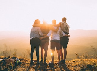 four person hands wrap around shoulders while looking at sunset