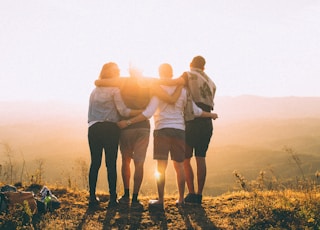 four person hands wrap around shoulders while looking at sunset