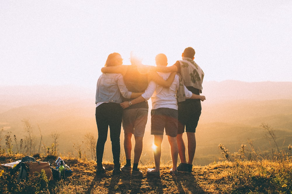 four person hands wrap around shoulders while looking at sunset