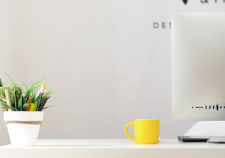 yellow ceramic mug beside gray aluminum iMac