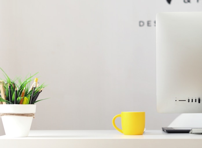 yellow ceramic mug beside gray aluminum iMac