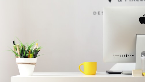A calm, minimalist workspace with a laptop and a cup of tea beside a small plant.