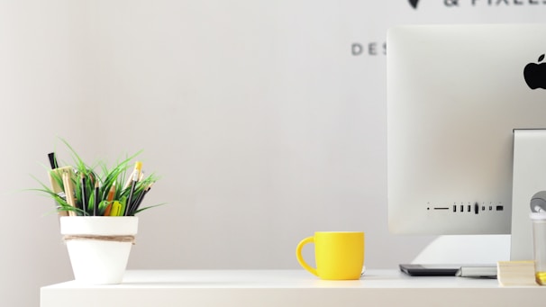 Minimalist workspace with a laptop, a cup of coffee, and a small plant on a white desk.