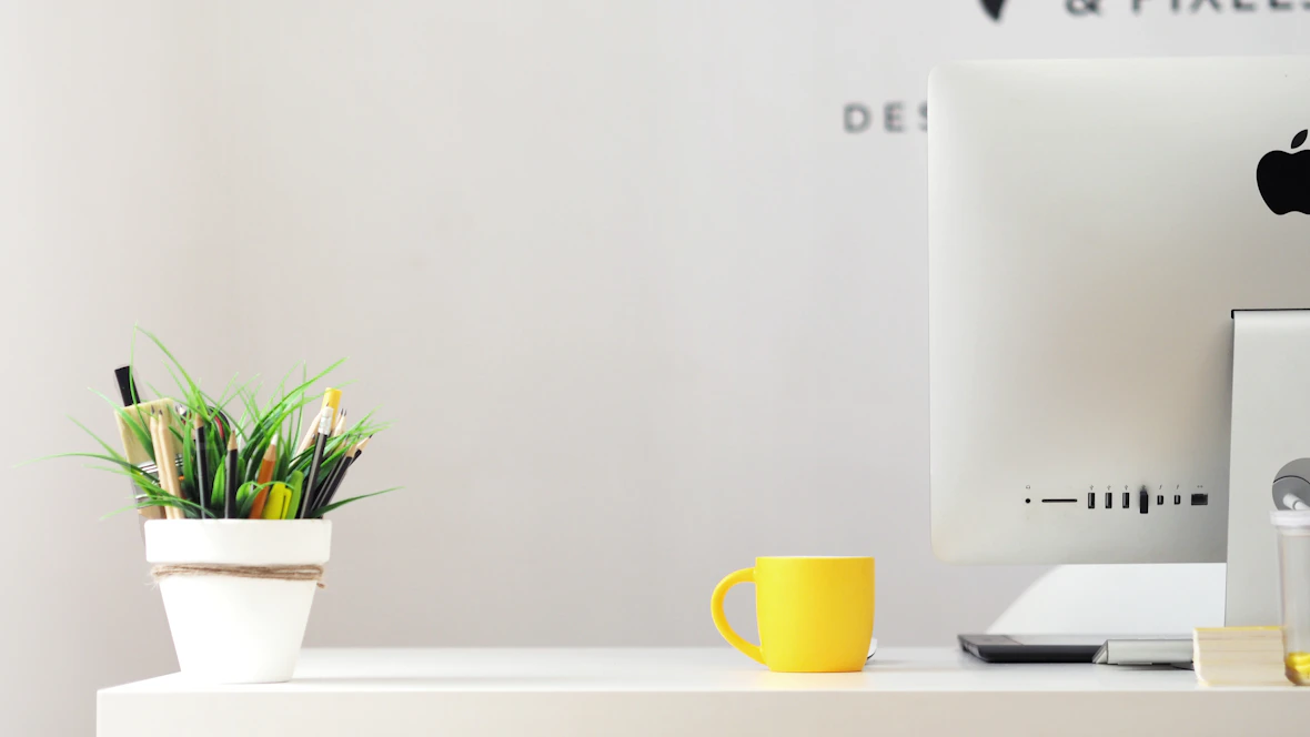 A calm, minimalist workspace with a laptop, a mint green plant pot, and a clean white desk.