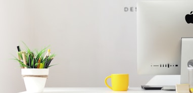 yellow ceramic mug beside gray aluminum iMac