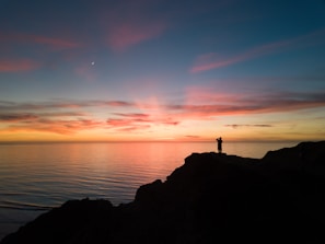 A joyful traveler standing on a cliff overlooking a vibrant sunset over the ocean